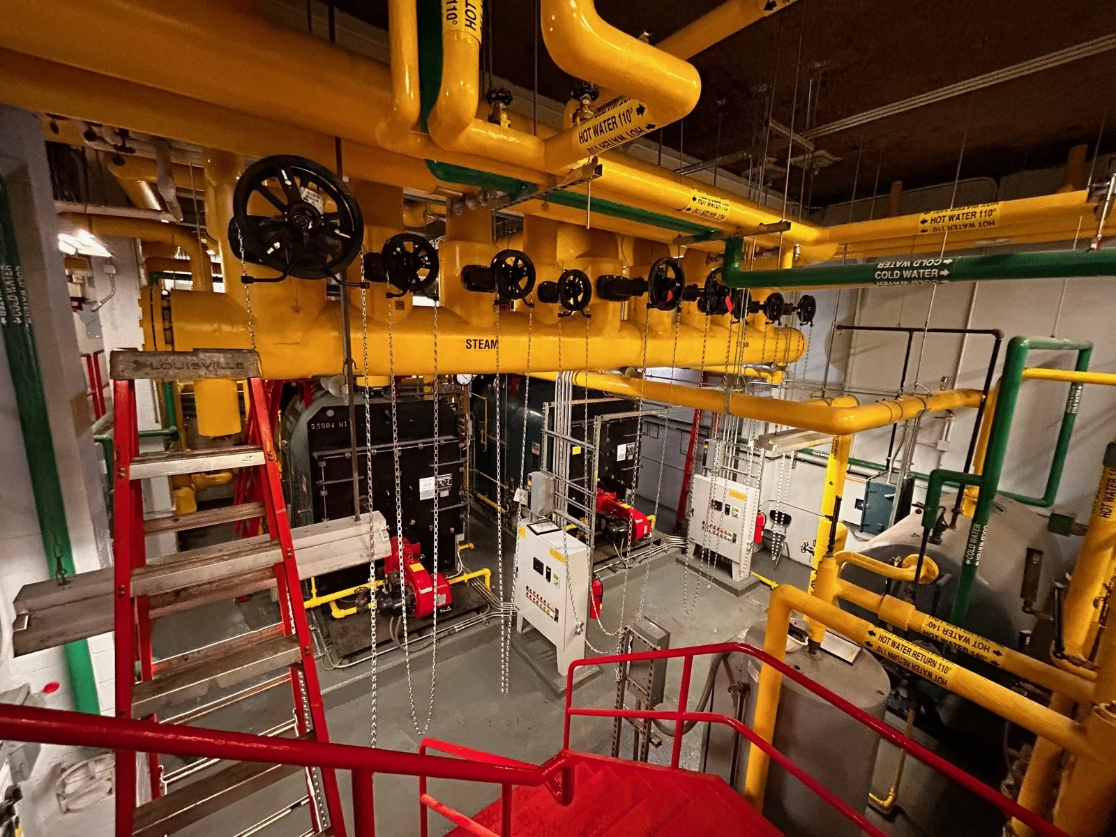 Mechanical room with steam and hot water piping, a critical infrastructure element evaluated by CPM Scheduling Consultants for project timelines.